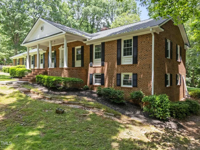 a view of a brick house with a small yard plants and large tree