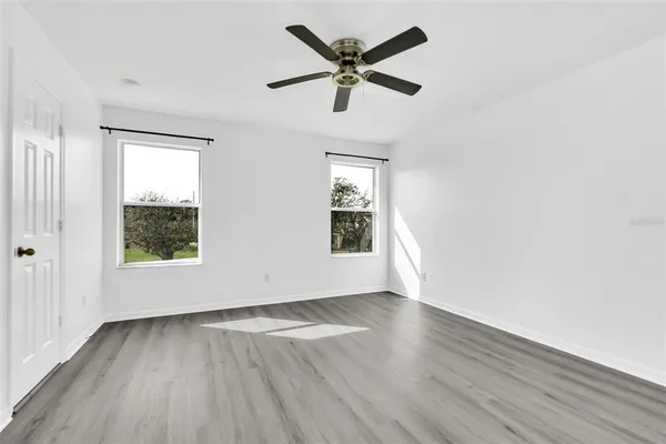 an empty room with wooden floor fan and windows