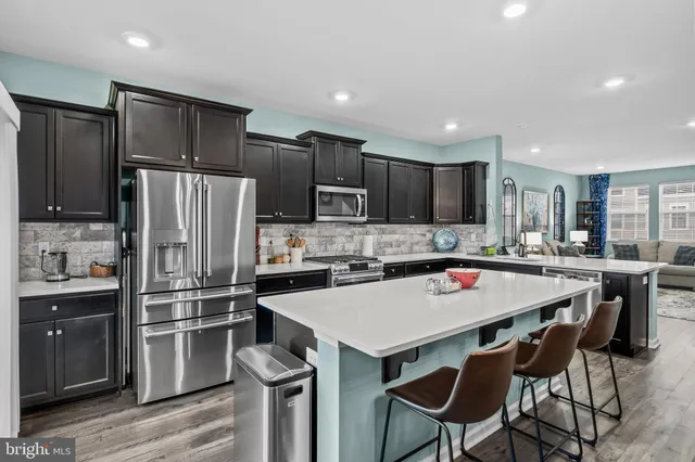 a kitchen with stainless steel appliances kitchen island granite countertop a sink dishwasher a refrigerator and cabinets with wooden floor