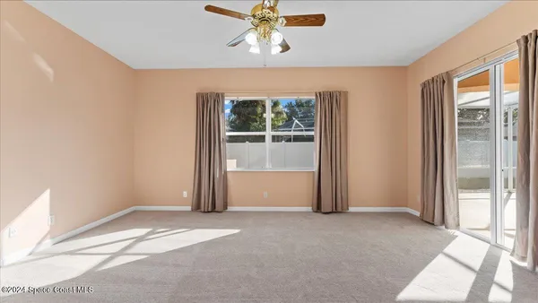 an empty room with chandelier fan and windows