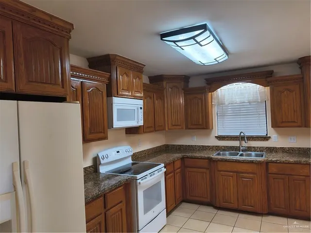 a kitchen with granite countertop a sink a stove a refrigerator a microwave oven with cabinets and wooden floor