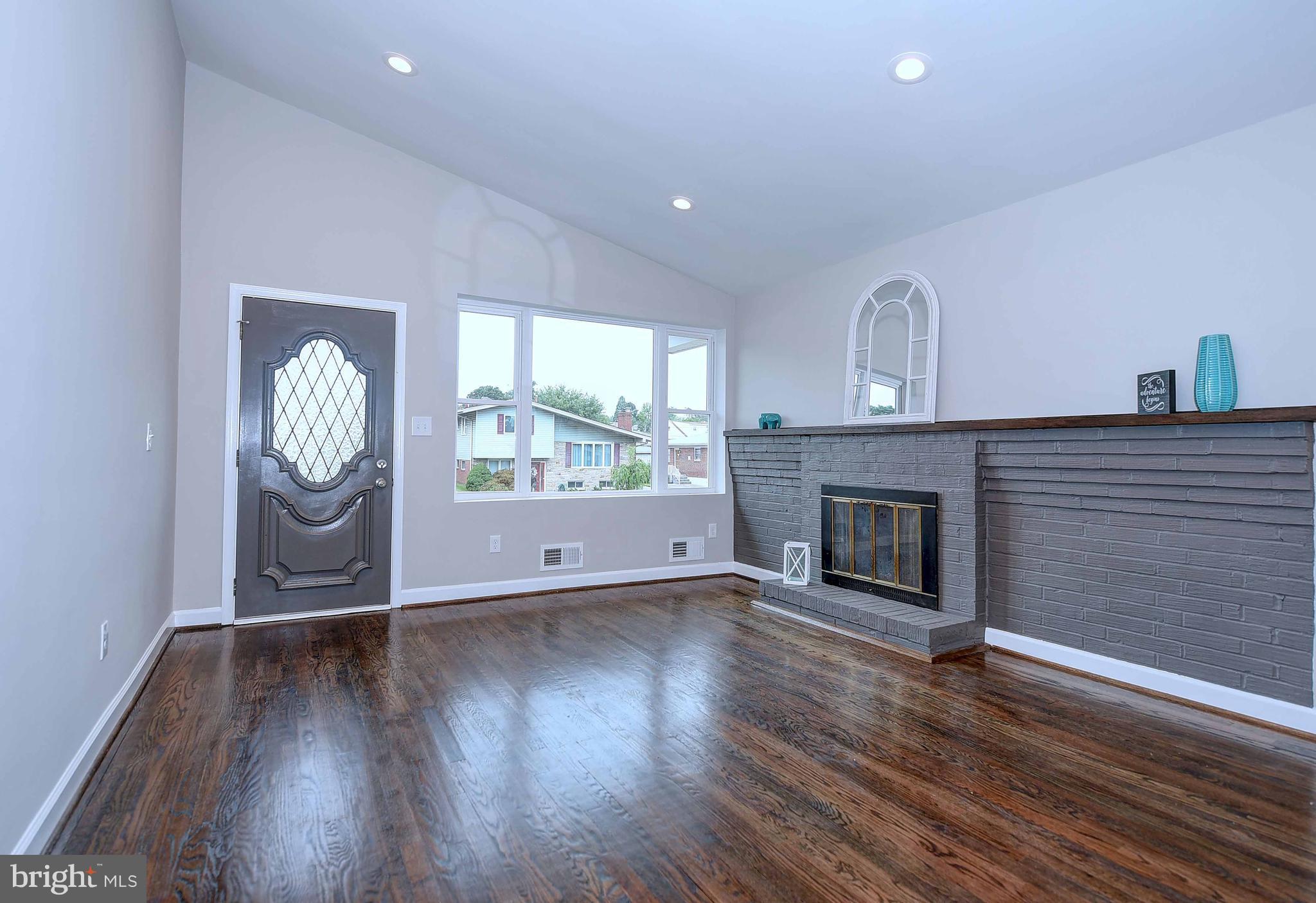 1213 Ridgeshire Road Baltimore, MD 21222 - Photo 7 of 30 an empty room with wooden floor fireplace and windows