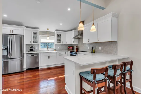 a kitchen with stainless steel appliances granite countertop a sink a stove a refrigerator and island with wooden floor