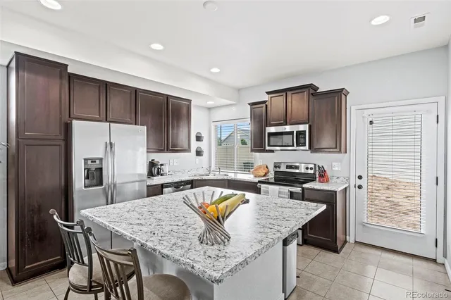 a kitchen with stainless steel appliances granite countertop a refrigerator a stove a sink a dining table and chairs