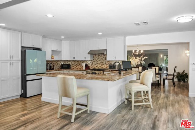 a kitchen with stainless steel appliances granite countertop a dining table chairs refrigerator sink and cabinets