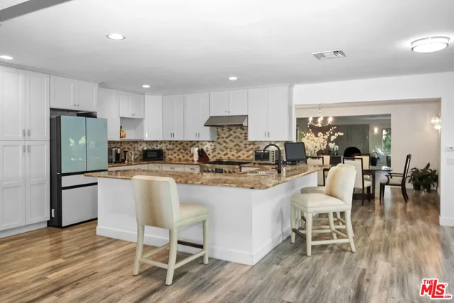 a kitchen with stainless steel appliances granite countertop a dining table chairs refrigerator sink and cabinets