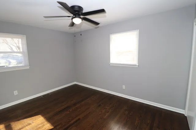 a view of an empty room with wooden floor and a ceiling fan