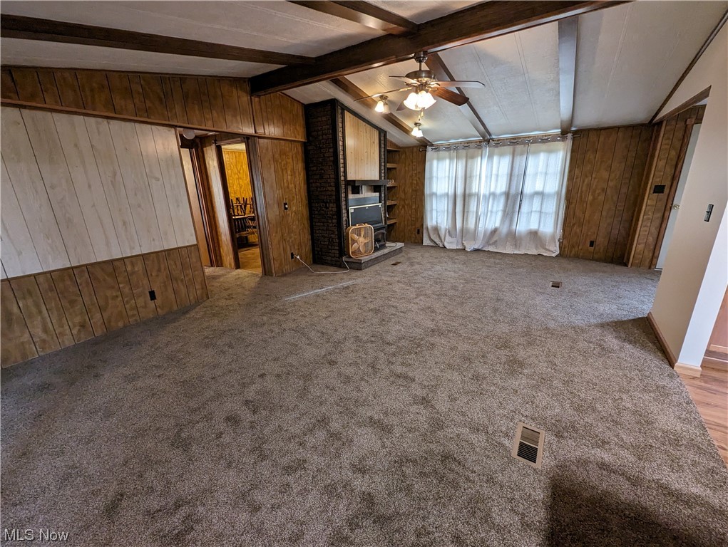 10267 Cable Line Road Newton Falls, OH 44444 - Photo 12 of 33 Unfurnished living room with light colored carpet, ceiling fan, vaulted ceiling with beams, a wood stove, and wooden walls