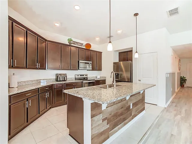 a open kitchen with kitchen island granite countertop a refrigerator oven a sink dishwasher and white cabinets with wooden floor