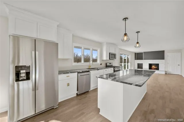 a kitchen with stainless steel appliances granite countertop a refrigerator a sink a stove and white cabinets