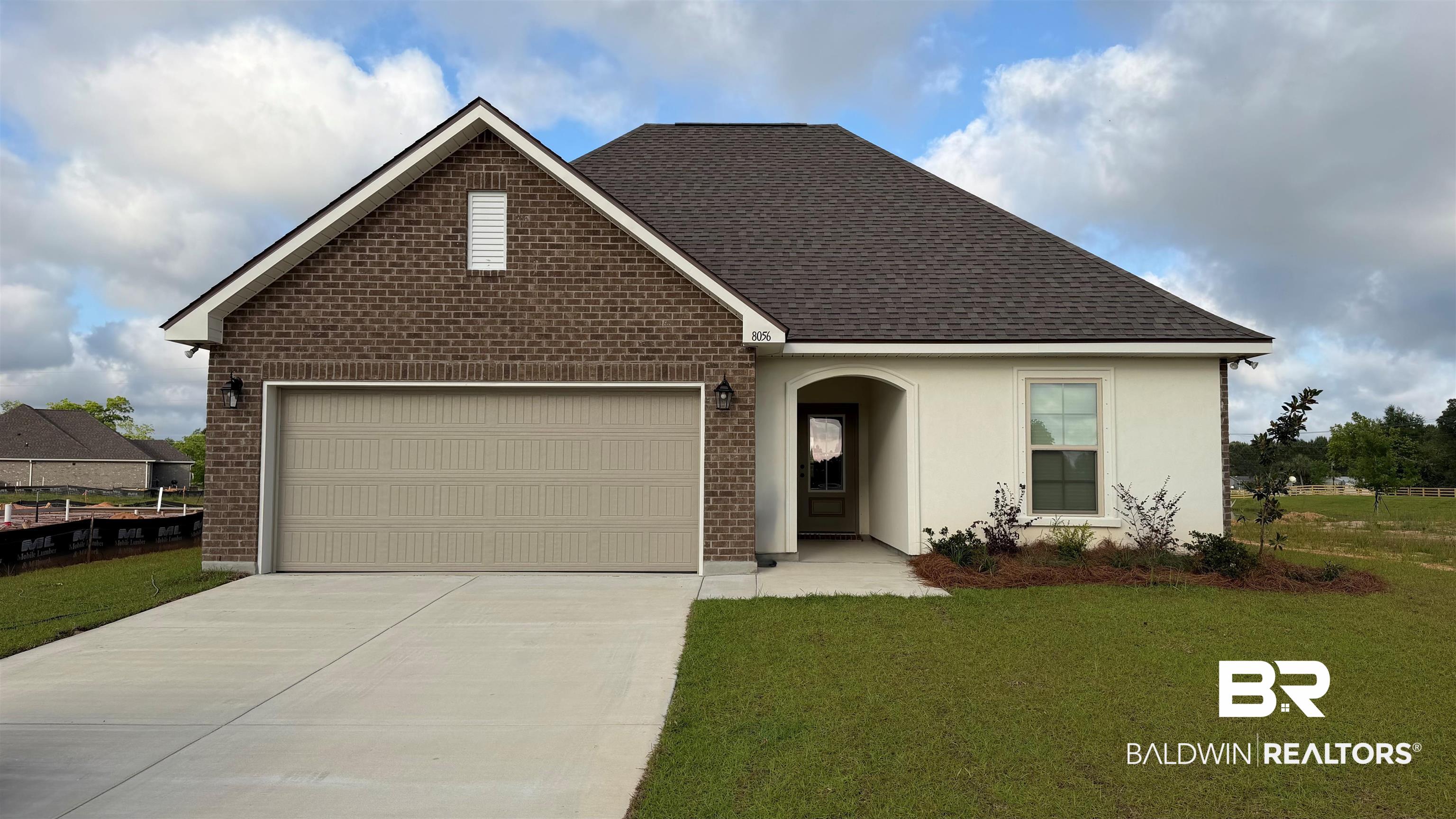 8056 Knoll Road Foley, AL 36535 - Photo 1 of 3 Brick and stucco exterior featuring a two-car garage, dark shingle roof, arched entry, and front landscaping