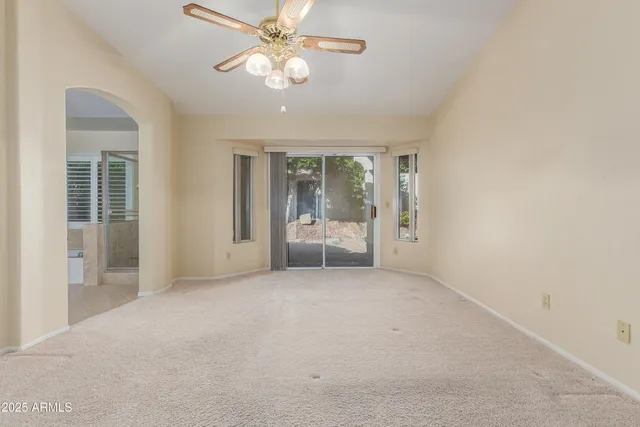 an empty room with chandelier fan and windows