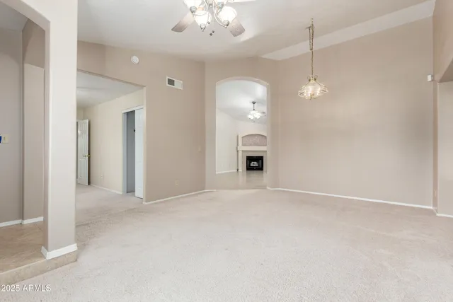 an empty room with kitchen view and a chandelier fan