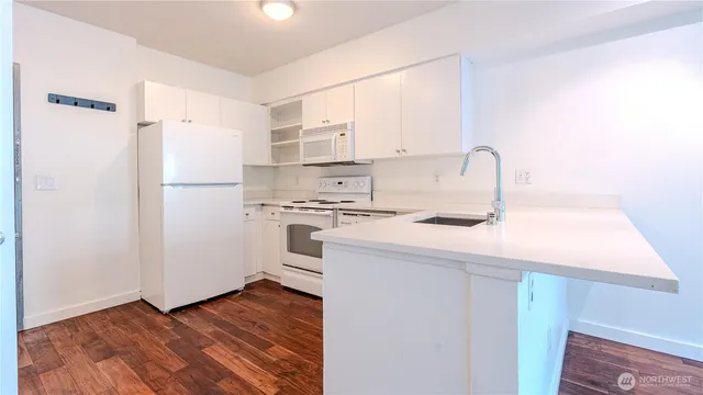 a kitchen with a refrigerator a stove a sink and white cabinets with wooden floor