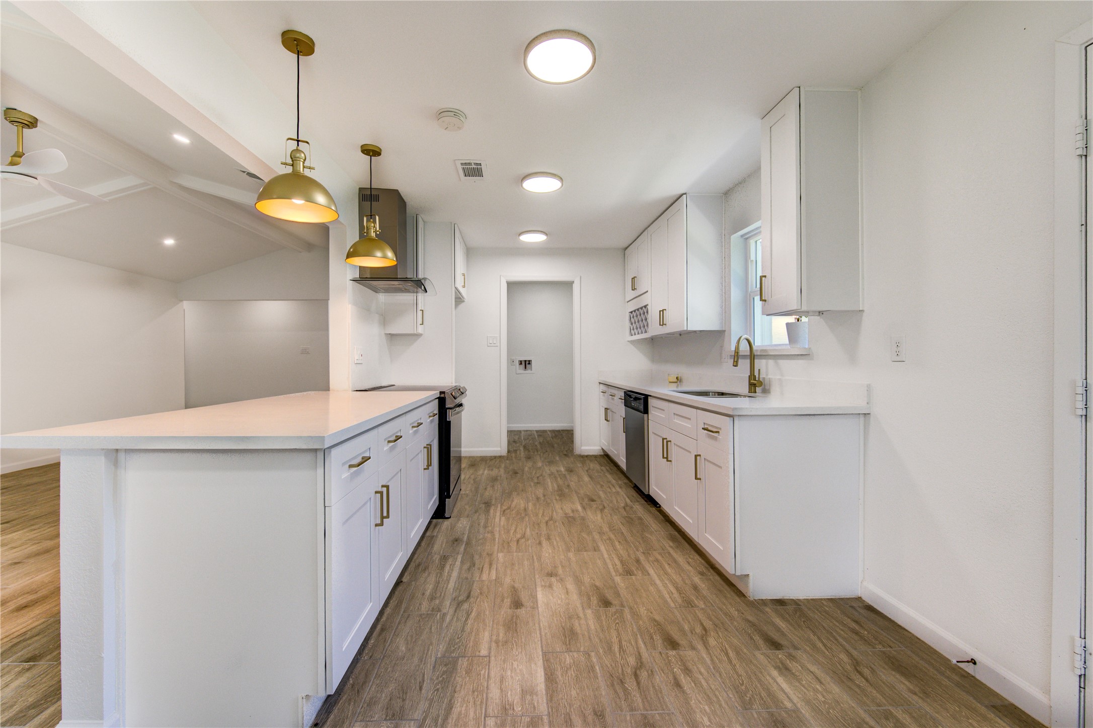 5411 Logston Lane Spring, TX 77389 - Photo 16 of 50 Sleek modern kitchen featuring white cabinetry, gold hardware, and stainless steel appliances, complemented by warm wood-look flooring and stylish pendant lighting.