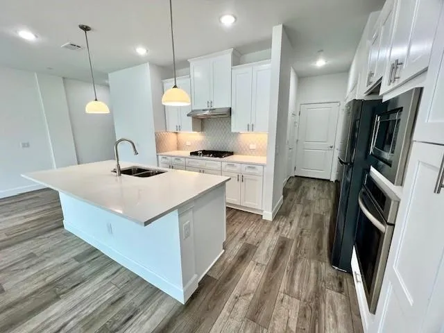 a view of a kitchen with kitchen island a sink wooden floor and stainless steel appliances