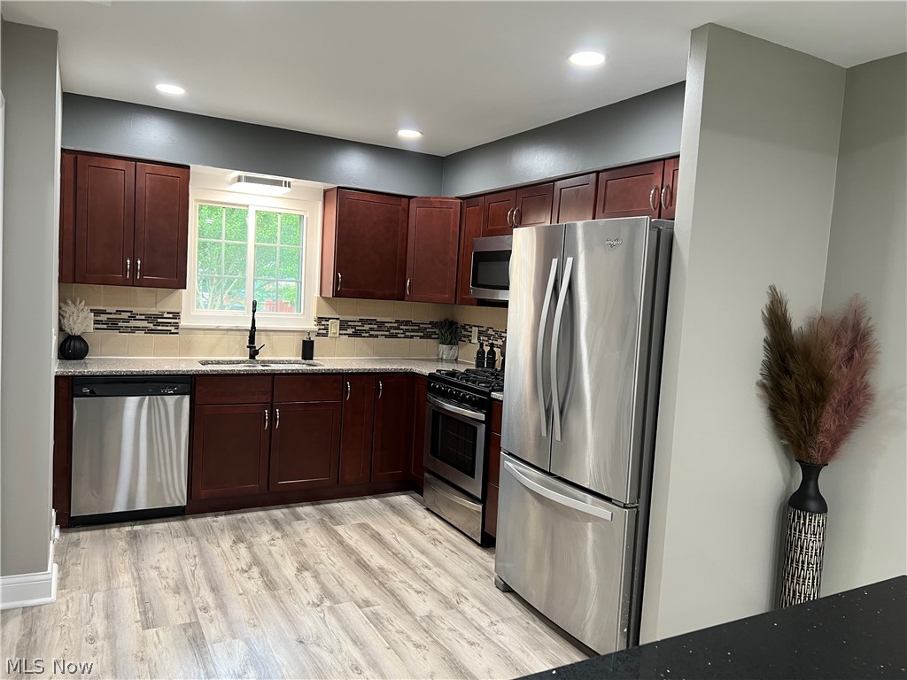 7475 Selwick Drive Parma, OH 44129 - Photo 8 of 29 Kitchen featuring light stone countertops, light hardwood / wood-style flooring, tasteful backsplash, sink, and appliances with stainless steel finishes