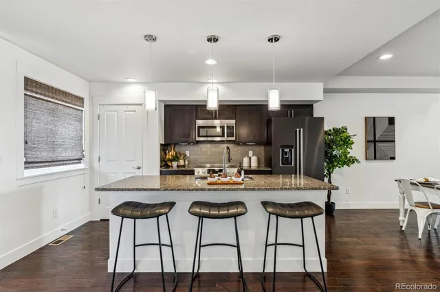a kitchen with stainless steel appliances kitchen island granite countertop a dining table chairs and a refrigerator