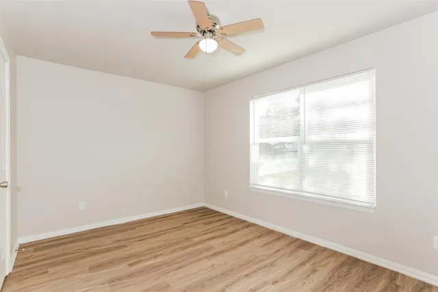 an empty room with wooden floor ceiling fan and windows