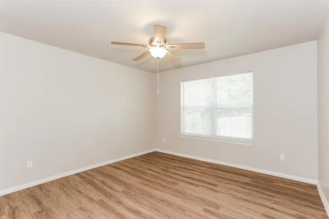 an empty room with wooden floor fan and windows