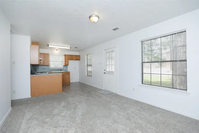a view of an empty room with kitchen and a window