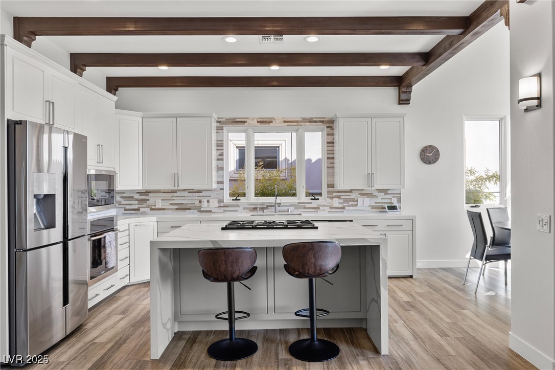 3 Rue Allard Way Henderson, NV 89011 - Photo 11 of 49 Kitchen with white cabinets, decorative backsplash, a kitchen island, appliances with stainless steel finishes, and a kitchen bar