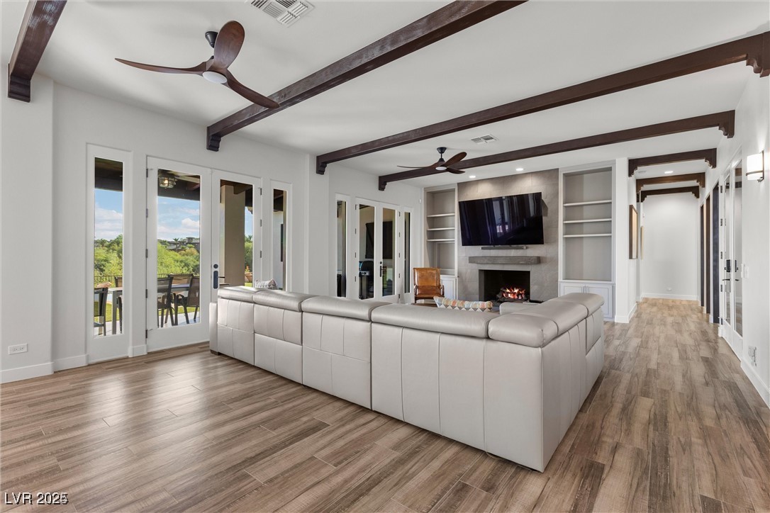 3 Rue Allard Way Henderson, NV 89011 - Photo 8 of 49 Unfurnished living room featuring a fireplace, wood finished floors, visible vents, a ceiling fan, and beam ceiling