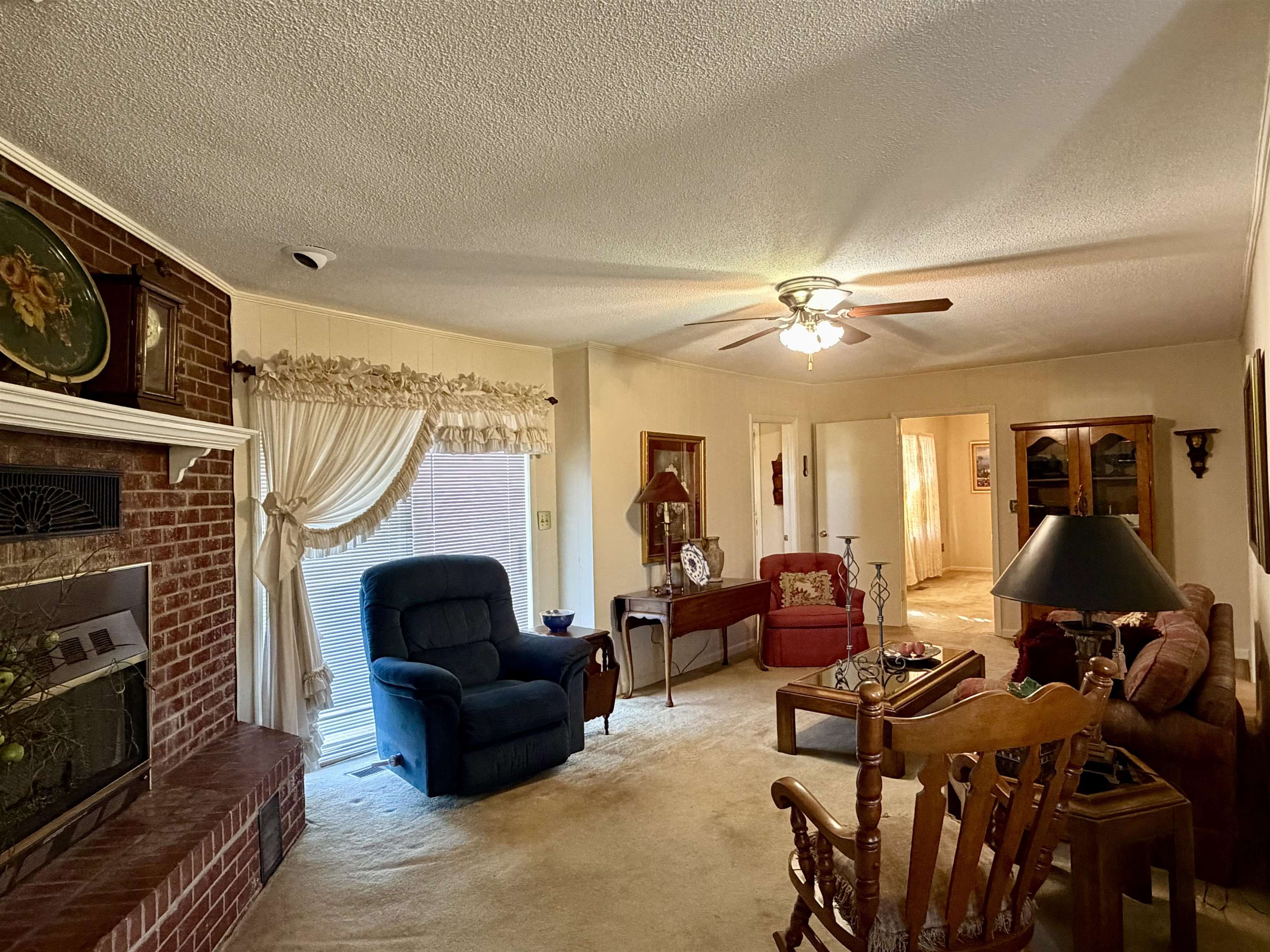 192 New Bethel Road Selmer, TN 38375 - Photo 14 of 27 Carpeted living room featuring a brick fireplace, a textured ceiling, and a ceiling fan