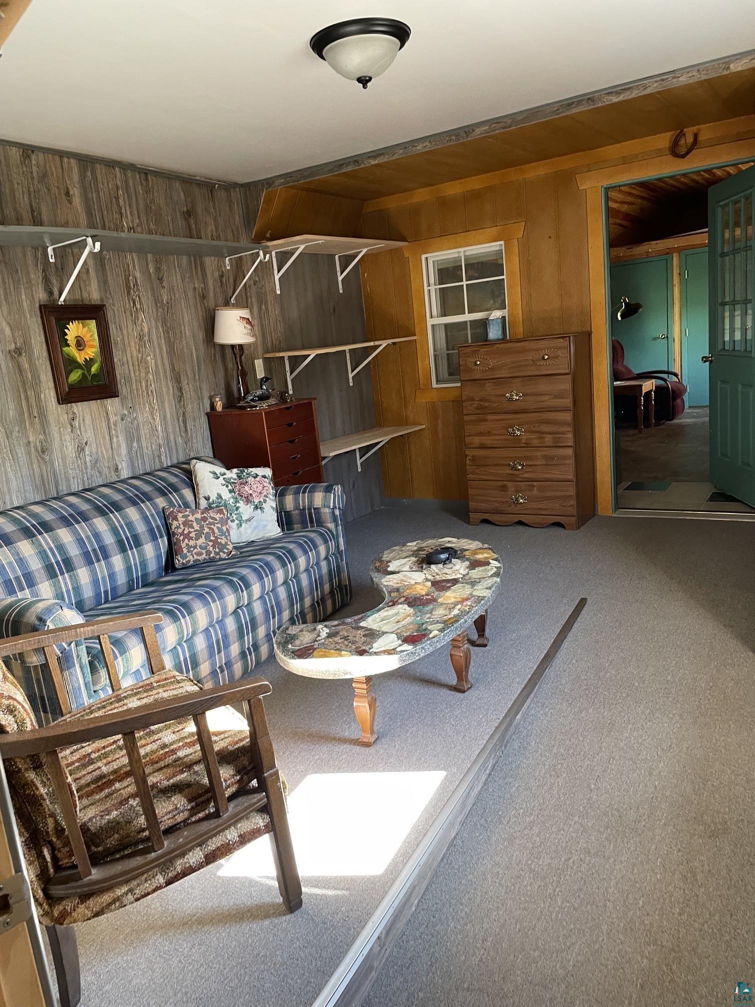 1152 Fernberg Road Ely, MN 55731 - Photo 13 of 24 Carpeted living area featuring wood-look wall paneling, a ceiling-mounted light fixture, and a window with wood trim
