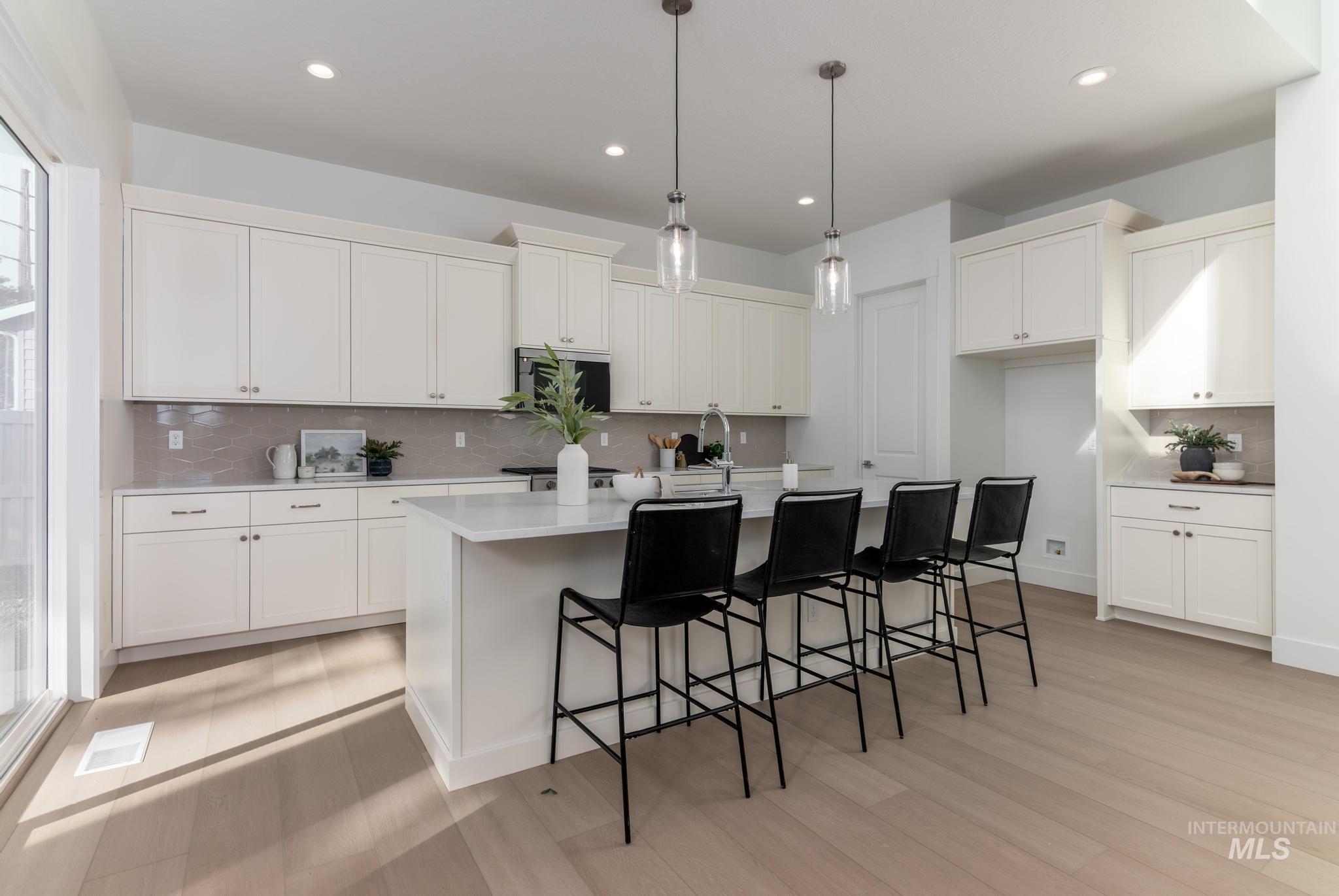 5431 North Ebony Way Meridian, ID 83646 - Photo 6 of 13 Kitchen featuring a kitchen bar, decorative light fixtures, an island with sink, decorative backsplash, and light wood-type flooring
