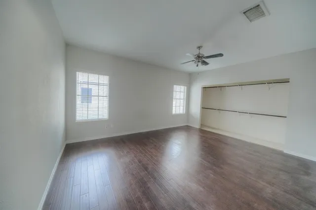 an empty room with wooden floor chandelier fan and windows