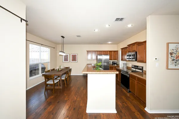 a kitchen with stainless steel appliances kitchen island granite countertop a stove a refrigerator a dining table and chairs with wooden floor