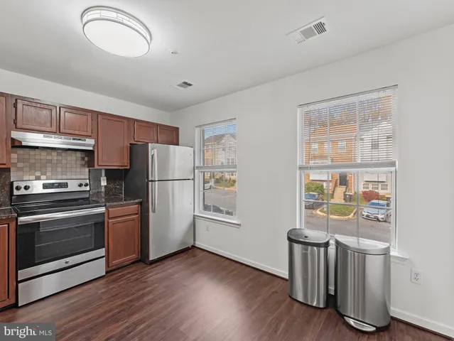 a kitchen with stainless steel appliances granite countertop a refrigerator a sink dishwasher a stove and a dining table with wooden floor