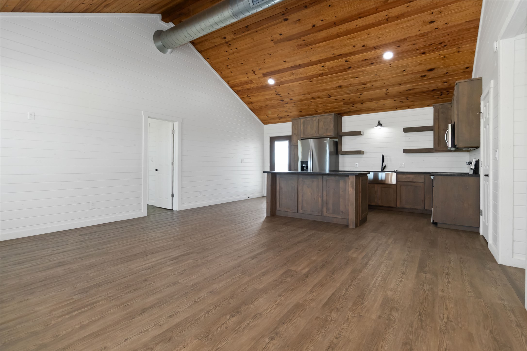 Kitchen featuring open shelves, a sink, dark countertops, dark wood finished floors, and stainless steel fridge