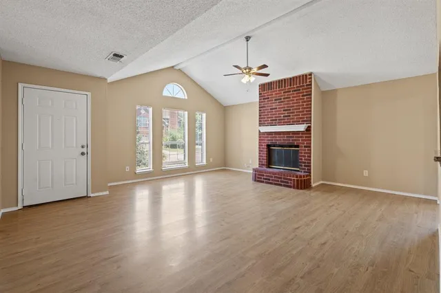 an empty room with wooden floor fireplace and windows
