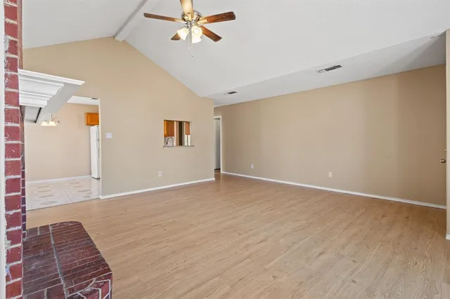 a view of an empty room with wooden floor and a ceiling fan