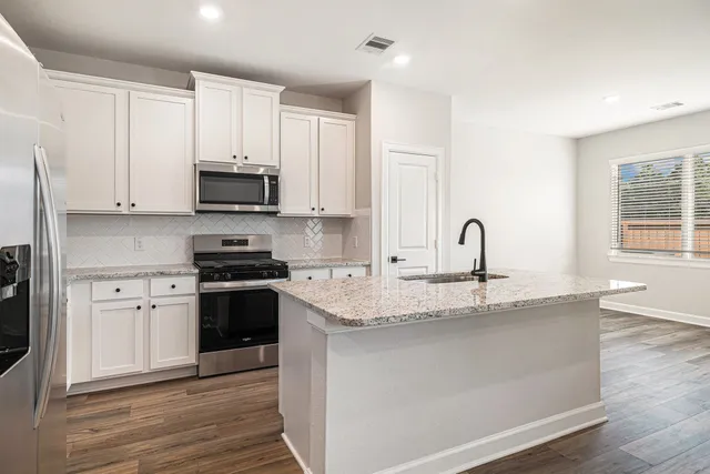 a kitchen with stainless steel appliances granite countertop a stove a sink and white cabinets