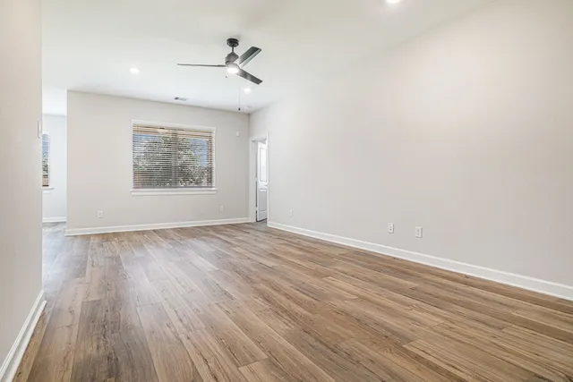an empty room with wooden floor chandelier fan and windows