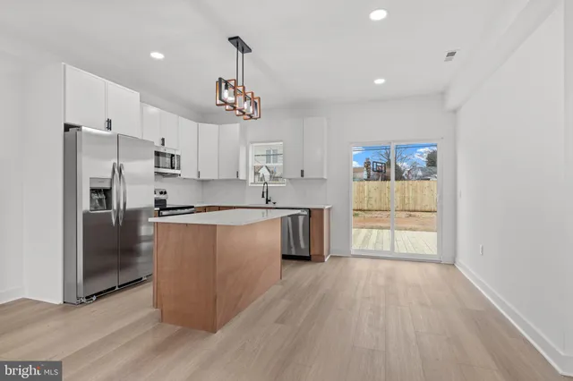 a kitchen with stainless steel appliances a refrigerator a sink dishwasher a stove and white cabinets with wooden floor