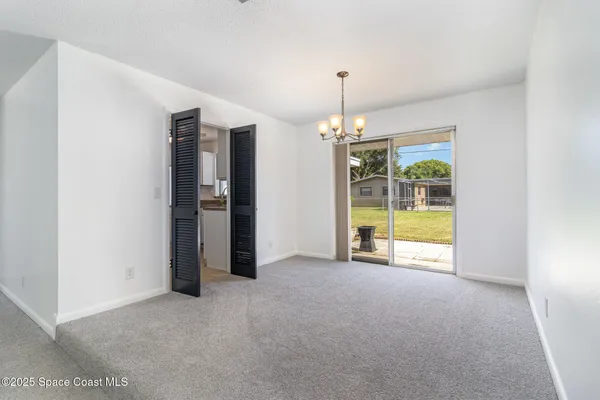 a view of an empty room with chandelier fan and kitchen view