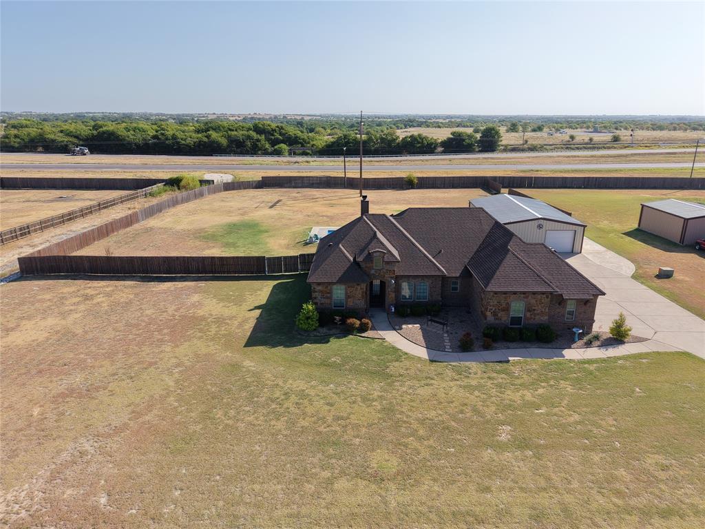123 Cactus Drive Decatur, TX 76234 - Photo 5 of 30 Brick residence situated on expansive acreage featuring a pitched roofline with dark shingle finish, multiple outbuildings including metal-frame structures, manicured lawn grounds, and established tree line bordering the property perimeter.