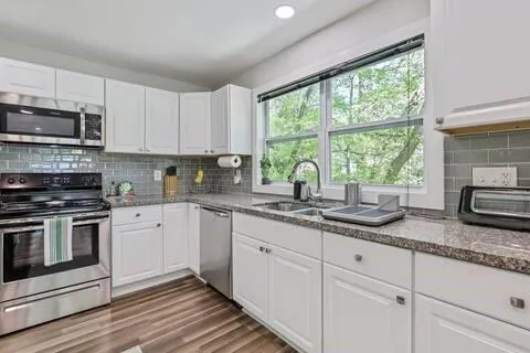 a kitchen with granite countertop white cabinets stainless steel appliances a sink and a window