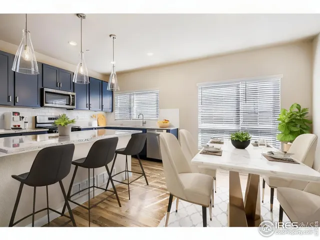 a kitchen with stainless steel appliances kitchen island granite countertop a dining table chairs and a refrigerator