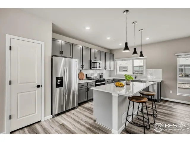 a kitchen with stainless steel appliances kitchen island granite countertop a refrigerator a stove a sink a dining table and chairs with wooden floor