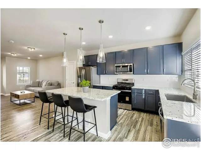a kitchen with stainless steel appliances kitchen island granite countertop a stove a sink a refrigerator a dining table and chairs with wooden floor