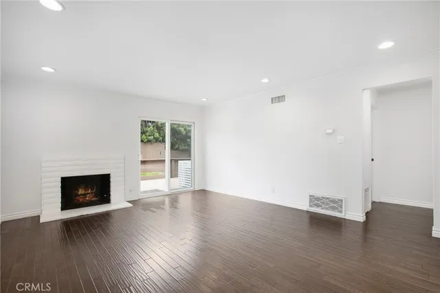 a view of an empty room with wooden floor fireplace and a window
