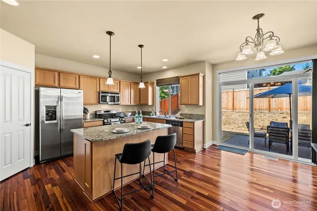 a kitchen with stainless steel appliances granite countertop a refrigerator a oven a sink dishwasher and a dining table with wooden floor