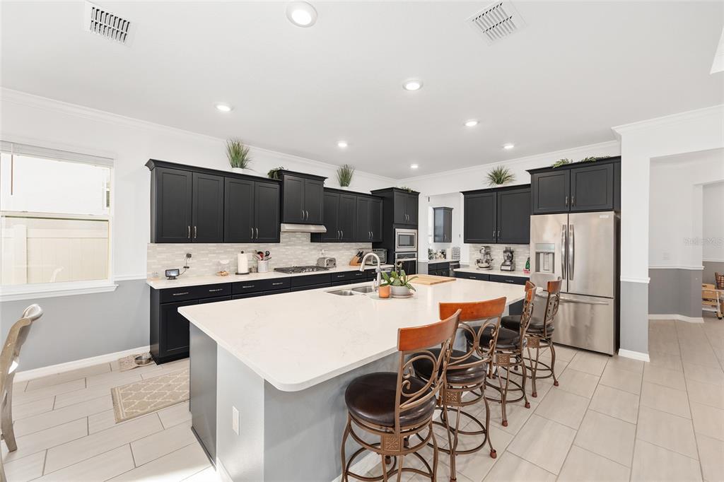 7208 Southwest 65th Place Road Ocala, FL 34474 - Photo 23 of 76 a kitchen with stainless steel appliances kitchen island granite countertop a refrigerator a stove a sink a dining table and chairs with wooden floor