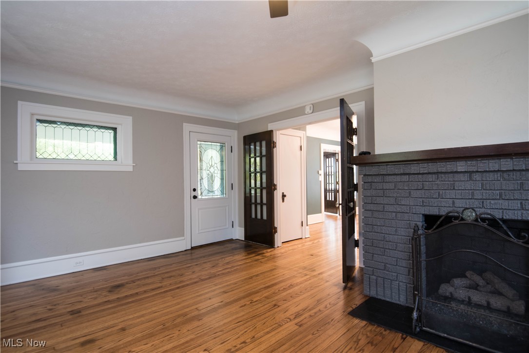 7003 Brecksville Road Independence, OH 44131 - Photo 7 of 35 Unfurnished living room featuring wood finished floors, ornamental molding, a brick fireplace, and ceiling fan
