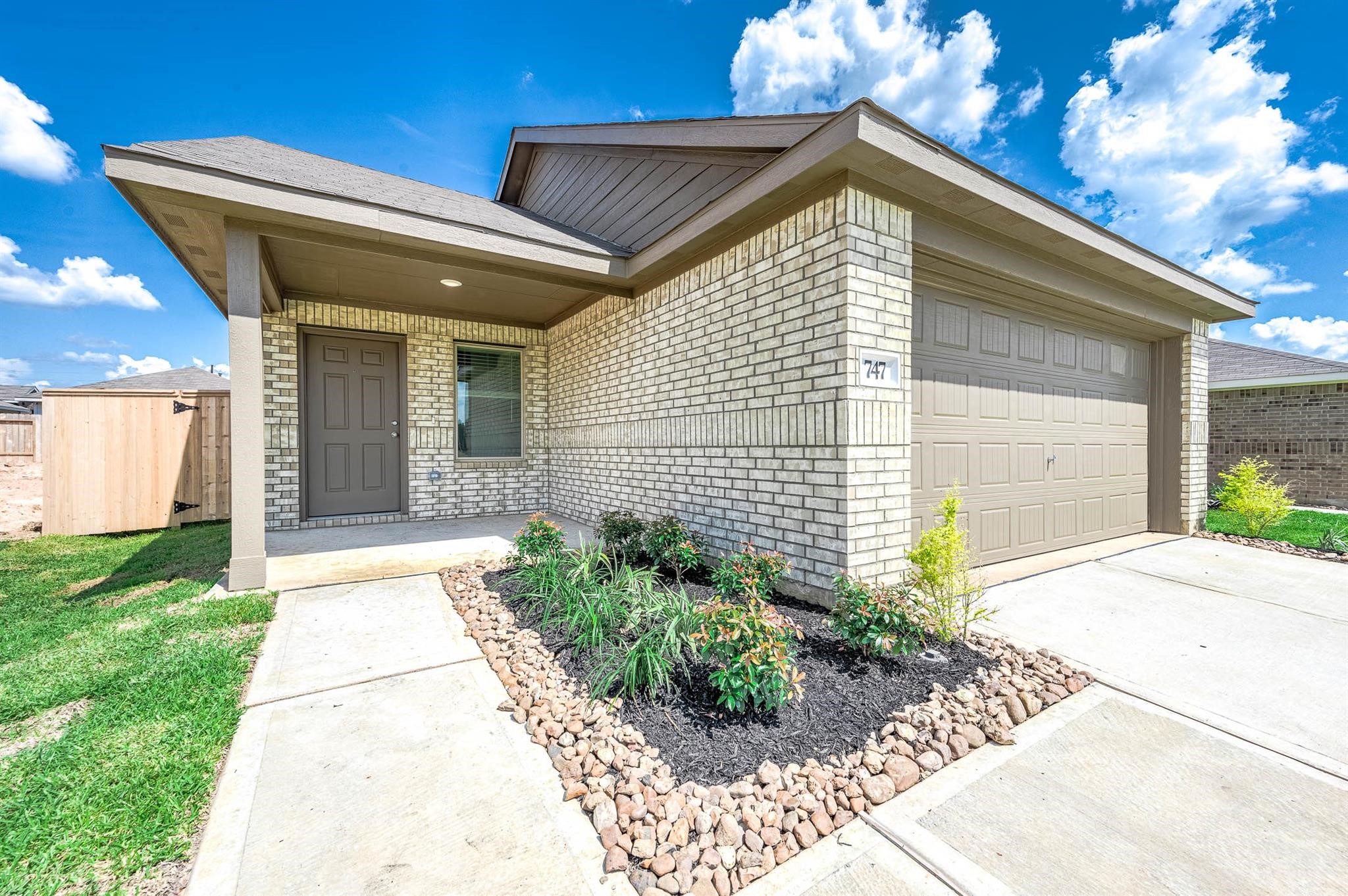 This is a modern single-story home featuring a brick exterior, a two-car garage, and a tidy front yard with landscaping. The entryway is sheltered by a porch, providing a welcoming entrance.